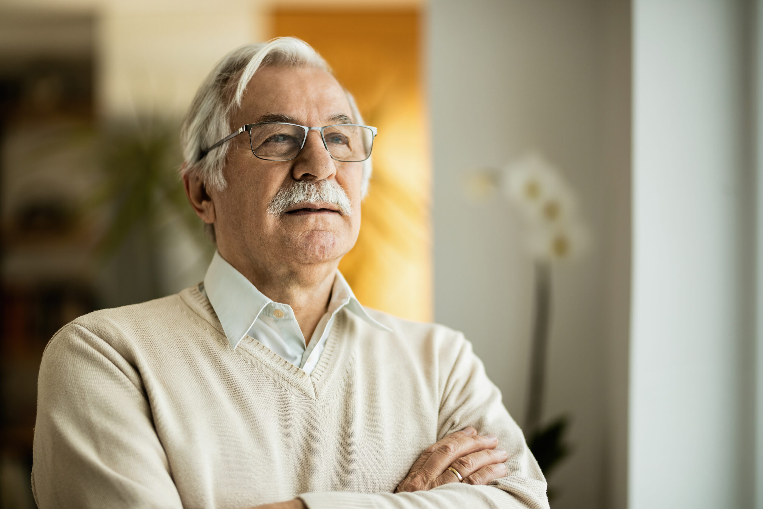 Portrait of mature man contemplating while standing with arms crossed at home.